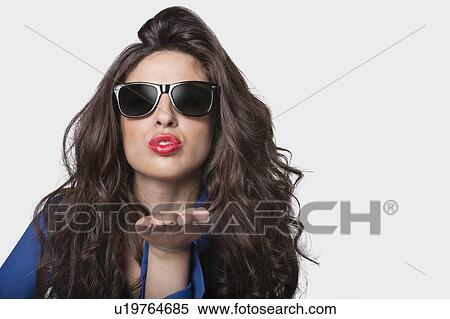 Stock Photography - Portrait of a young woman in sunglasses blowing a kiss over gray background. Fotosearch
