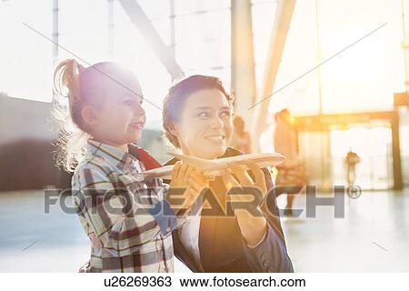 Stock Image - Portrait of airport staff holding airplane toy while playing with cute little girl in airport. Fotosearch