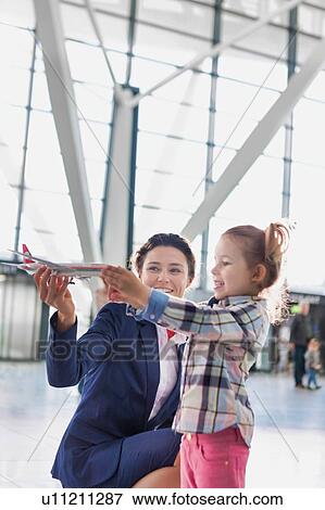Stock Photo - Portrait of airport staff holding airplane toy while playing with cute little girl in airport. Fotosearch