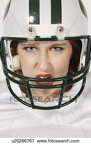 Stock Photo - Portrait of an aggressive young woman in football uniform against gray background. Fotosearch