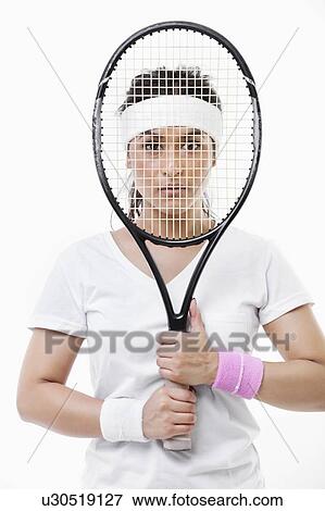 Stock Photo - Portrait of an Asian young woman looking through tennis racket over white background. Fotosearch