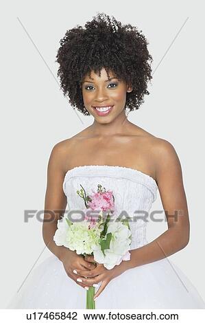 Stock Image - Portrait of an attractive African American bride holding bouquet over gray background. Fotosearch
