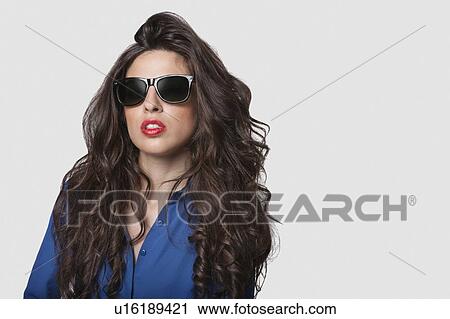 Stock Image - Portrait of an attractive young woman wearing sunglasses against gray background. Fotosearch
