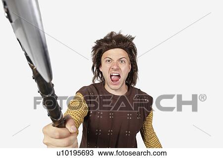Stock Image - Portrait of angry man in caveman costume holding axe against gray background. Fotosearch