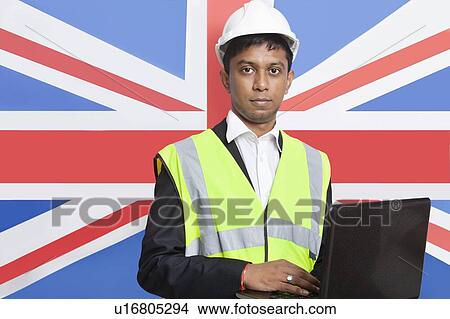 Picture - Portrait of Asian architect in reflective vest using laptop against British flag. Fotosearch