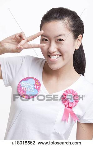 Stock Image - Portrait of Asian woman gesturing peace sign against white background. Fotosearch
