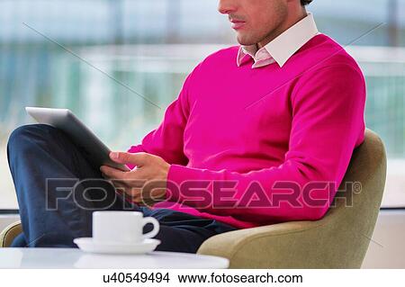 Portrait of attractive businessman using digital tablet while sitting and drinking coffee in lobby View Large Photo Image Picture - Portrait of attractive businessman using digital tablet while sitting and drinking coffee in lobby. Fotosearch