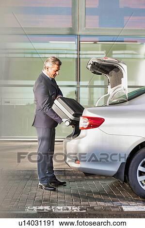 Portrait of attractive businessman putting his suitcase on a car trunk View Large Photo Image Stock Image - Portrait of attractive businessman putting his suitcase on a car trunk . Fotosearch