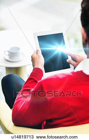 Stock Image - Portrait of attractive businessman using digital tablet while sitting and drinking coffee in lobby. Fotosearch