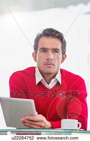 Stock Image - Portrait of attractive businessman using digital tablet while sitting and drinking coffee in lobby. Fotosearch