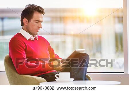 Portrait of attractive businessman using digital tablet while sitting and drinking coffee in lobby View Large Photo Image Stock Image - Portrait of attractive businessman using digital tablet while sitting and drinking coffee in lobby. Fotosearch