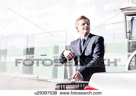 Portrait of attractive businessman putting his suitcase on a car trunk View Large Photo Image Stock Photo - Portrait of attractive businessman putting his suitcase on a car trunk . Fotosearch