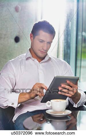 Portrait of attractive businessman using digital tablet while sitting and drinking coffee in lobby View Large Photo Image Stock Photograph - Portrait of attractive businessman using digital tablet while sitting and drinking coffee in lobby. Fotosearch