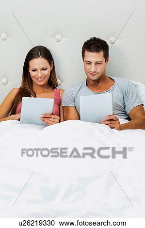 Stock Image - Portrait of attractive couple playing games using digital tablet on bed . Fotosearch