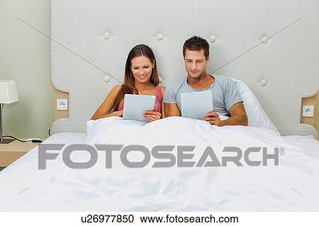 Stock Image - Portrait of attractive couple playing games using digital tablet on bed . Fotosearch