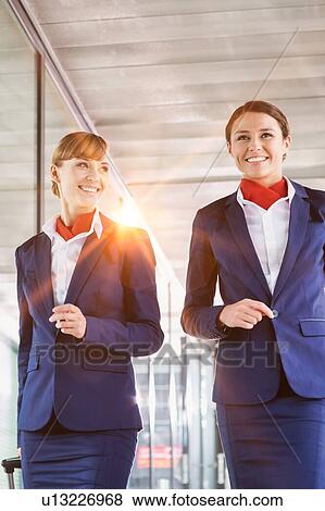 Stock Photo - Portrait of attractive flight attendants walking with their suitcase in airport. Fotosearch