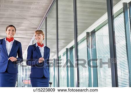 Stock Photo - Portrait of attractive flight attendants walking with their suitcase in airport. Fotosearch