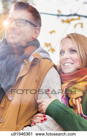 Stock Image - Portrait of attractive man and woman standing in park with lens flare . Fotosearch