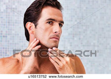 Stock Image - Portrait of attractive man checking his face in the mirror. Fotosearch