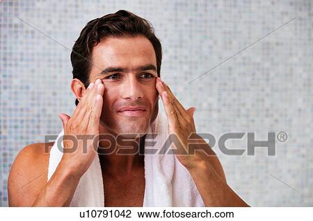 Stock Image - Portrait of attractive man cleansing his face with facial foam in the bathroom. Fotosearch