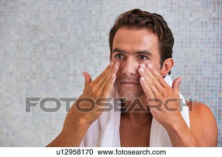 Stock Image - Portrait of attractive man cleansing his face with facial foam in the bathroom. Fotosearch