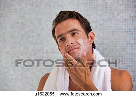 Stock Image - Portrait of attractive man cleansing his face with facial foam in the bathroom. Fotosearch