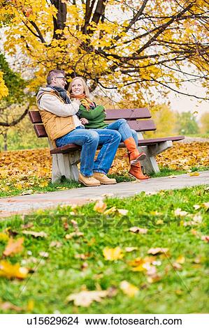 Picture - Portrait of attractive man sitting on bench while talking to his beautiful wife in park. Fotosearch