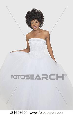 Picture - Portrait of beautiful African American bride in white wedding dress standing against plain background. Fotosearch