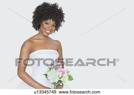 Stock Photo - Portrait of beautiful African American bride holding bouquet over gray background. Fotosearch