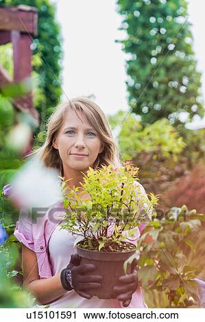Stock Image - Portrait of beautiful gardener carrying flower pot. Fotosearch