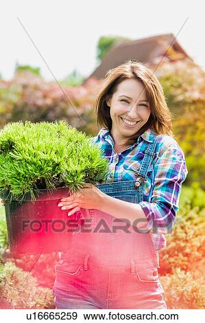 Stock Photo - Portrait of beautiful gardener carrying flower pot. Fotosearch
