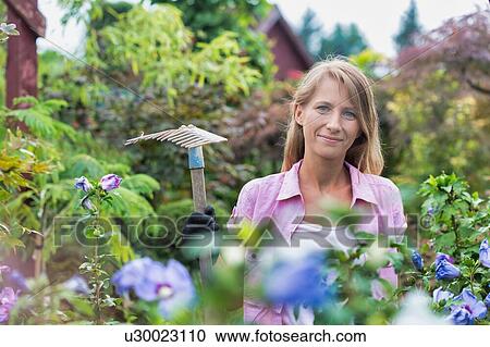 Stock Image - Portrait of beautiful gardener holding fork rake . Fotosearch