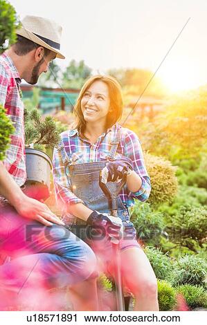 Stock Image - Portrait of beautiful gardener smiling while talking to coworker in shop. Fotosearch