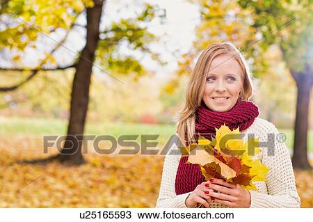 Stock Image - Portrait of beautiful woman holding maple leaves in park. Fotosearch