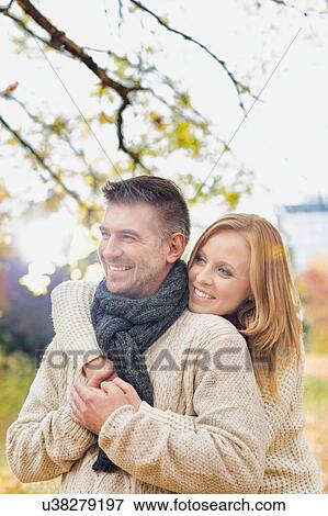 Stock Photo - Portrait of beautiful woman hugging her husband from behind in park. Fotosearch