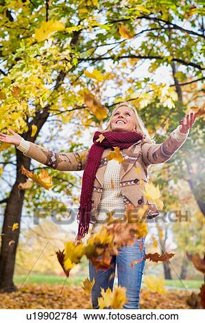 Picture - Portrait of beautiful woman playing with maple leaves in park. Fotosearch