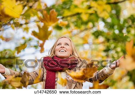 Stock Image - Portrait of beautiful woman playing with maple leaves in park. Fotosearch
