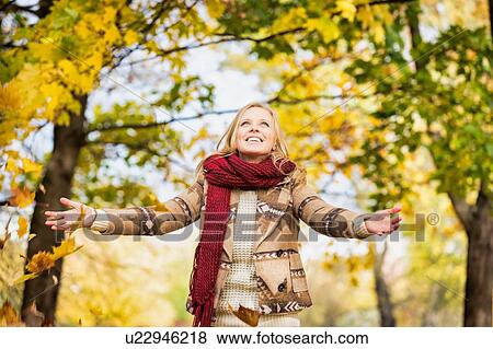 Stock Photo - Portrait of beautiful woman playing with maple leaves in park. Fotosearch