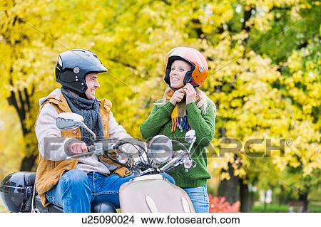 Portrait of beautiful woman putting her helmet on while husband is waiting to drive in park View Large Photo Image Picture - Portrait of beautiful woman putting her helmet on while husband is waiting to drive in park. Fotosearch