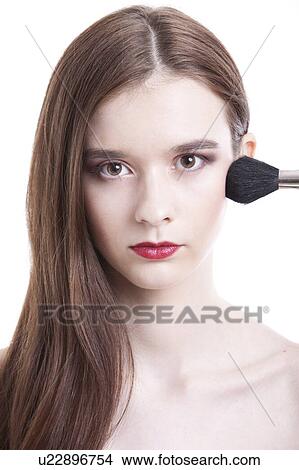 Picture - Portrait of beautiful young woman with red lips applying makeup against white background. Fotosearch