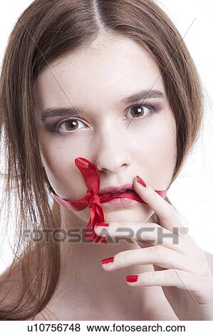 Stock Photo - Portrait of beautiful young woman with red ribbon tied over mouth against white background. Fotosearch