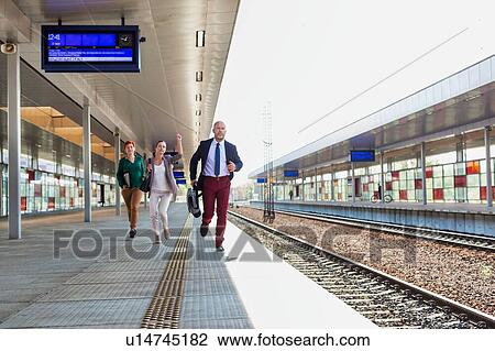 Stock Image - Portrait of business people running to catch the train in station. Fotosearch