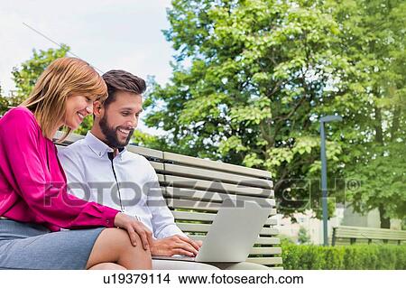 Picture - Portrait of businessman and businesswoman sitting on bench while working on laptop. Fotosearch