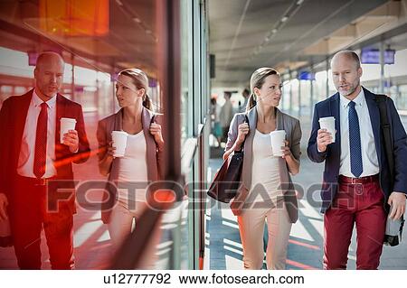 Stock Image - Portrait of businessman and businesswoman holding cup of coffee while walking and talking . Fotosearch