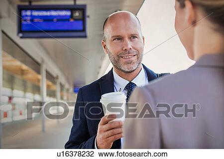 Stock Image - Portrait of businessman and businesswoman holding cup of coffee while talking and waiting for the train. Fotosearch