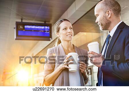 Portrait of businessman and businesswoman holding cup of coffee while talking and waiting for the train View Large Photo Image Stock Image - Portrait of businessman and businesswoman holding cup of coffee while talking and waiting for the train. Fotosearch