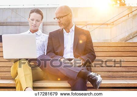 Portrait of businessman and businesswoman sitting on bench while discussing plans View Large Photo Image Stock Photo - Portrait of businessman and businesswoman sitting on bench while discussing plans. Fotosearch