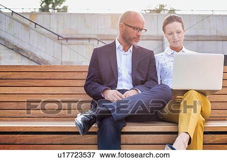 Stock Photo - Portrait of businessman and businesswoman sitting on bench while discussing plans. Fotosearch