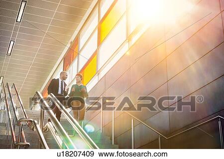 Stock Photo - Portrait of businessman and businesswoman talking while walking down stairs. Fotosearch
