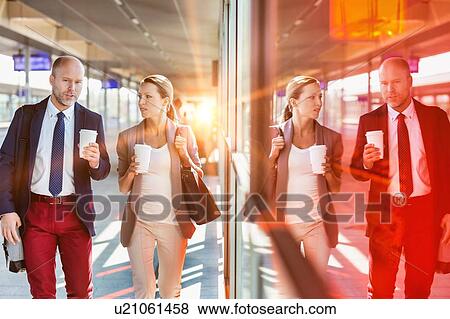 Stock Photo - Portrait of businessman and businesswoman holding cup of coffee while walking and talking . Fotosearch